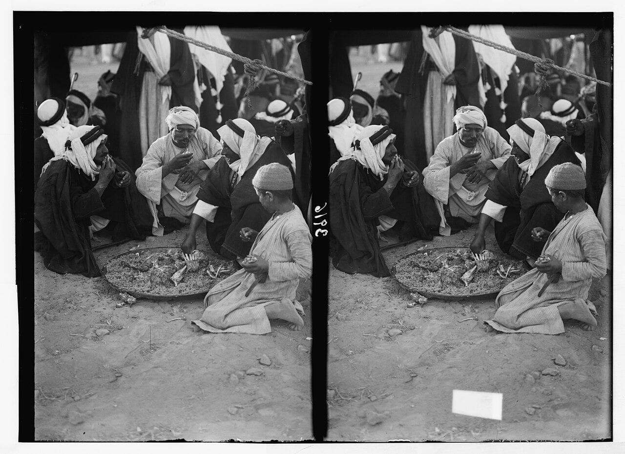 Bedouin men sharing rice and mutton at a feast in Bir al-Saba', 1930